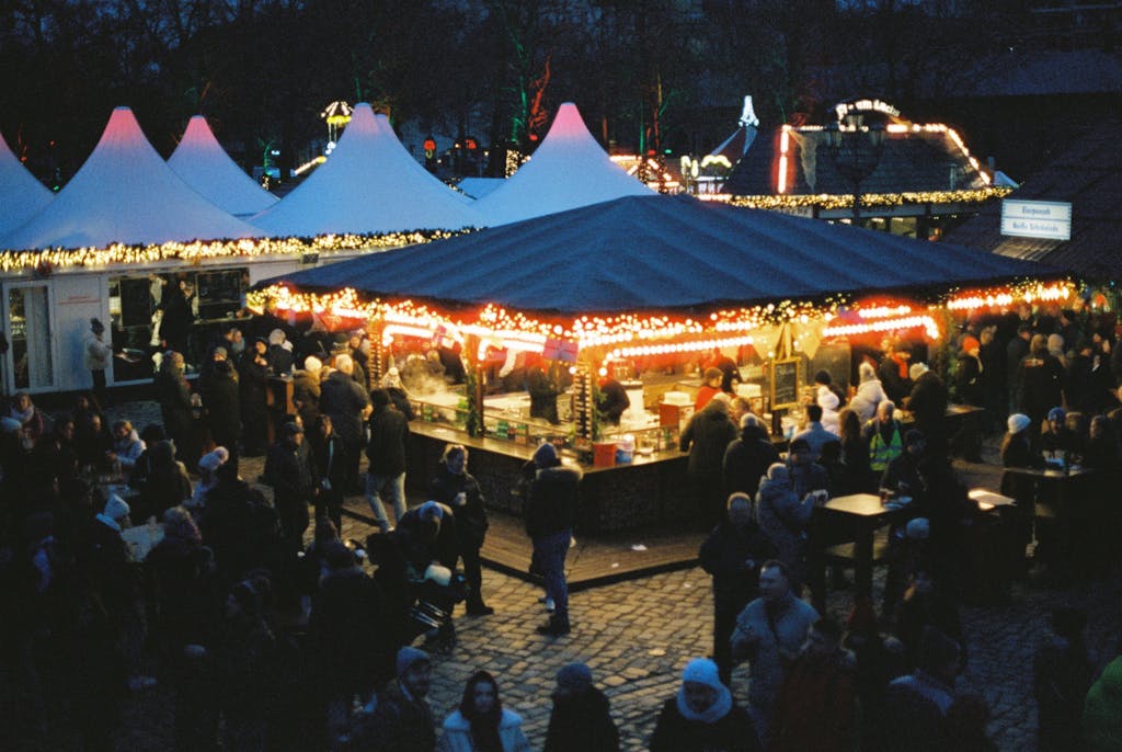 Colorful and bustling Christmas market in Berlin, Germany, showcasing festive lights and a lively crowd at night.