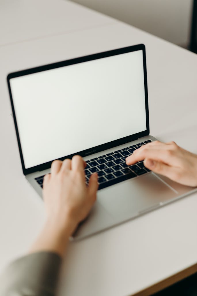 Close-up of hands typing on a laptop with a blank screen in a modern workspace.